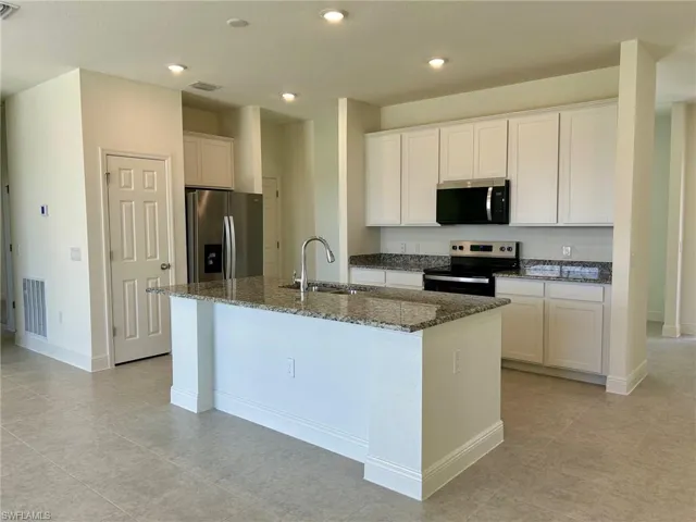 Kitchen with appliances with stainless steel finishes, a sink, a center island with sink, dark stone countertops, and white cabinets