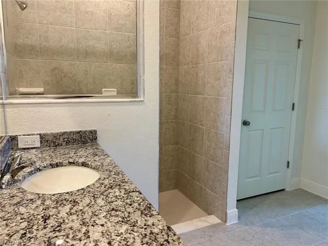 Full bathroom featuring a tile shower, baseboards, tile patterned flooring, and vanity