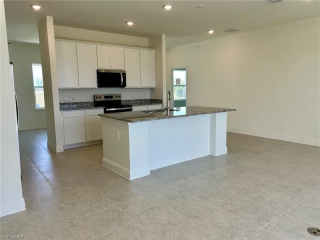 Kitchen with appliances with stainless steel finishes, a sink, dark stone countertops, white cabinets, and recessed lighting