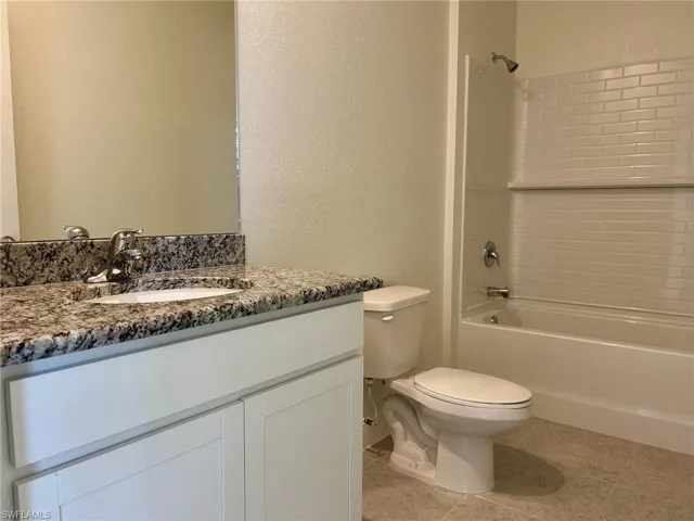 Full bathroom with vanity, toilet, shower / bathtub combination, a textured wall, and tile patterned floors