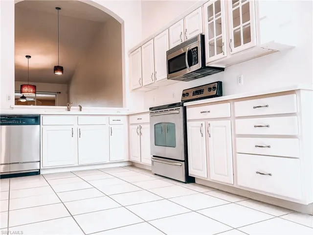 Kitchen with stainless steel appliances, pendant lighting, light tile floors, sink, and white cabinets