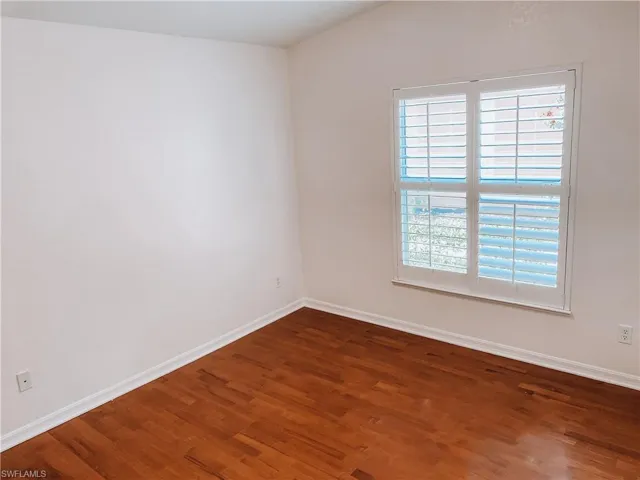 Spare room with plenty of natural light, vaulted ceiling, and dark wood-type flooring