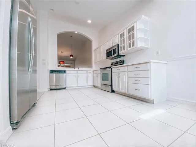 Kitchen with appliances with stainless steel finishes, white cabinets, pendant lighting, sink, and light tile flooring