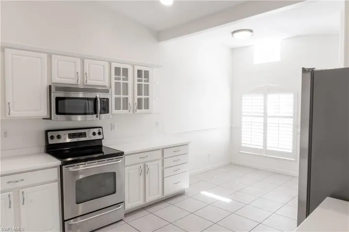 Kitchen with stainless steel appliances, vaulted ceiling with beams, white cabinets, and light tile flooring