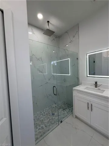 Bathroom with vanity, a marble finish shower, and light marble finish flooring
