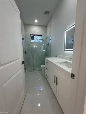 Full bath with vanity, a marble finish shower, and light marble finish floors