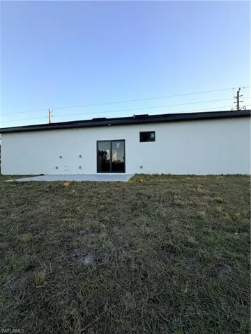 Rear view of property featuring a lawn and stucco siding