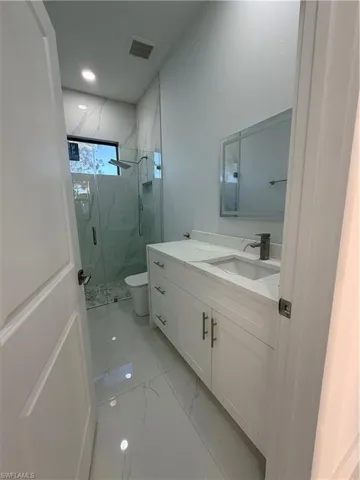 Full bath featuring vanity, a marble finish shower, and light marble finish floors