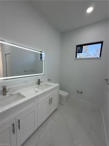 Bathroom featuring double vanity, light marble finish floors, and recessed lighting