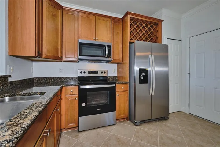 Kitchen with brown cabinets, stainless steel appliances, dark stone counters, ornamental molding, and light tile patterned floors