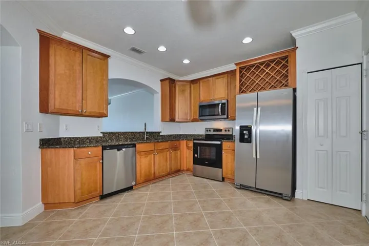 Kitchen with crown molding, stainless steel appliances, arched walkways, brown cabinetry, and light tile patterned flooring