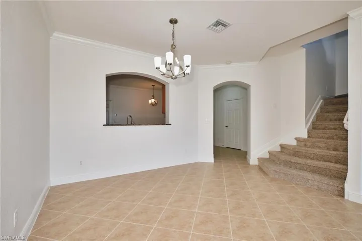 Spare room featuring crown molding, light tile patterned flooring, arched walkways, stairway, and a chandelier