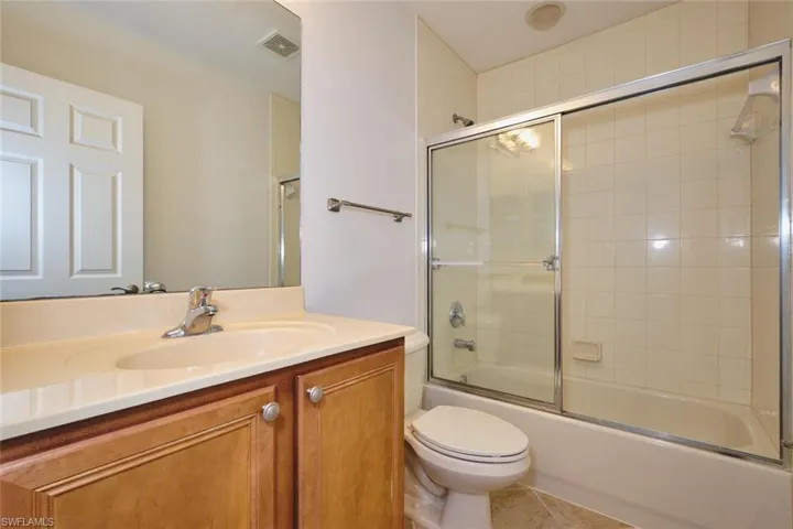 Bathroom with combined bath / shower with glass door, vanity, and tile patterned flooring