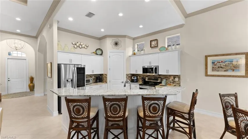 Kitchen featuring a breakfast bar area, white cabinetry, light stone countertops, and stainless steel appliances