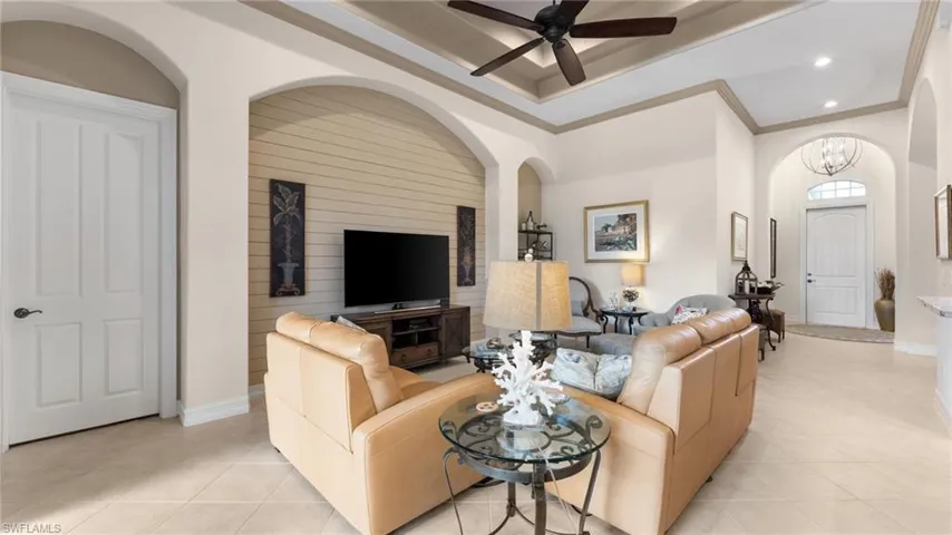 Living room featuring crown molding, light tile patterned flooring, and ceiling fan with notable chandelier