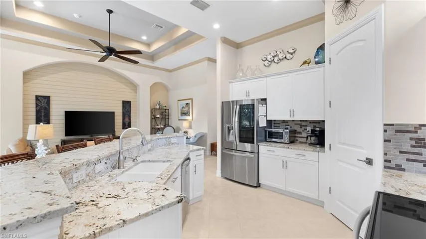 Kitchen featuring sink, stainless steel fridge with ice dispenser, an island with sink, light stone counters, and white cabinetry