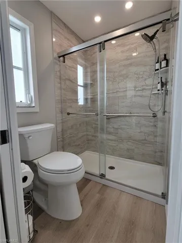 Bathroom featuring toilet, plenty of natural light, hardwood / wood-style floors, and a shower with shower door