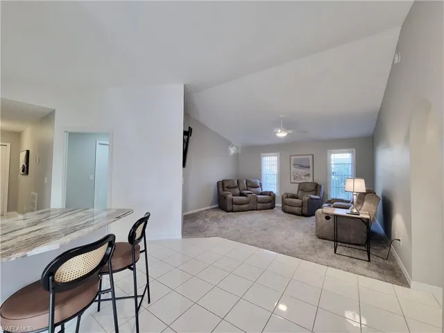 Living room with vaulted ceiling, light colored carpet, and ceiling fan