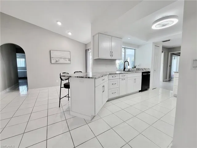 Kitchen featuring white cabinetry, light stone counters, light tile patterned floors, a kitchen breakfast bar, and kitchen peninsula
