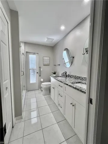 Main bathroom featuring vanity with dual sinks, toilet, and a shower with full glass shower door