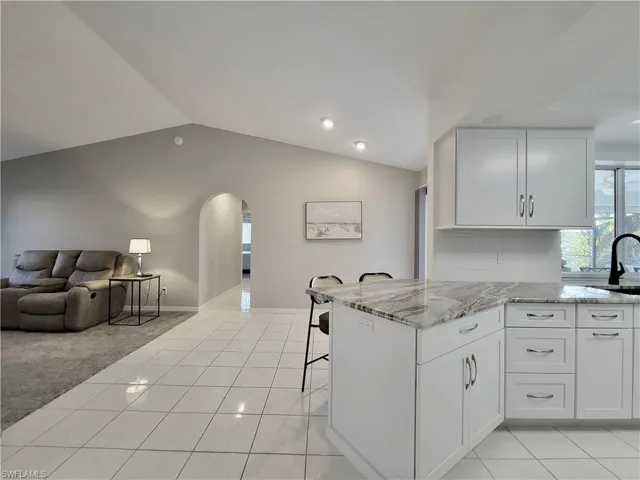 Living room or Great room pictured with Kitchen, lofted ceiling, a breakfast bar, and white cabinets with soft close drawers.