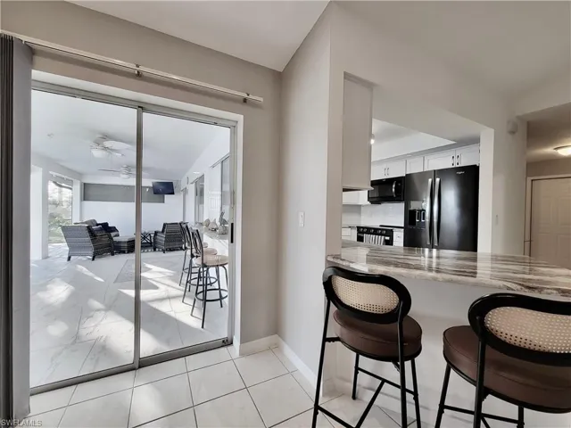 Kitchen featuring a breakfast bar, white cabinets, ceiling fan, stainless steel fridge with ice dispenser, and light stone countertops