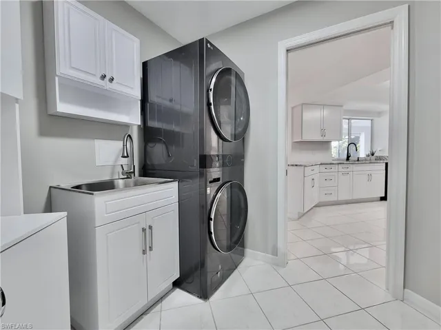 Washroom with cabinets, stacked washing maching and dryer, and sink