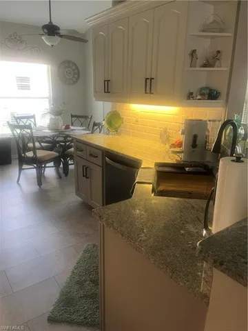 Kitchen featuring light cabinetry with dark hardware, a subway tile backsplash with under-cabinet lighting, granite countertops, and tile flooring