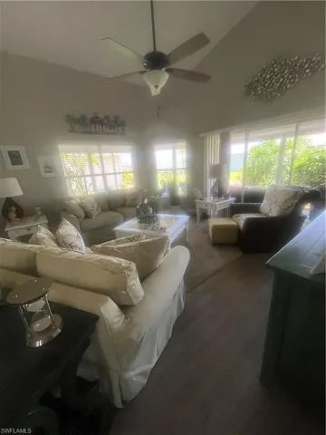 Living area featuring vaulted ceilings, a ceiling fan with integrated lighting, wood-finish flooring, and multiple windows with blinds
