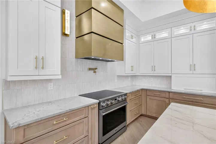 Kitchen featuring stainless steel range with electric cooktop, light stone countertops, glass insert cabinets, decorative backsplash, and white cabinets