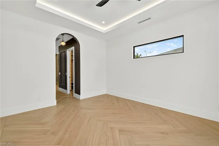 Unfurnished room with arched walkways, a tray ceiling, and ceiling fan