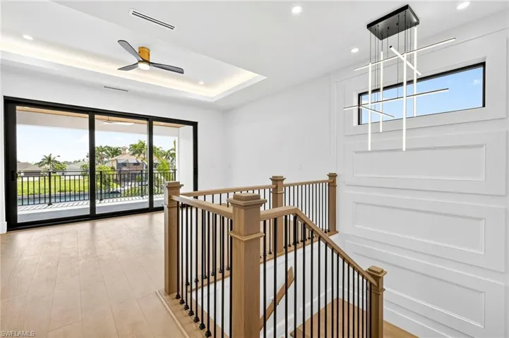 Hallway featuring an upstairs landing, light wood finished floors, a tray ceiling, and recessed lighting