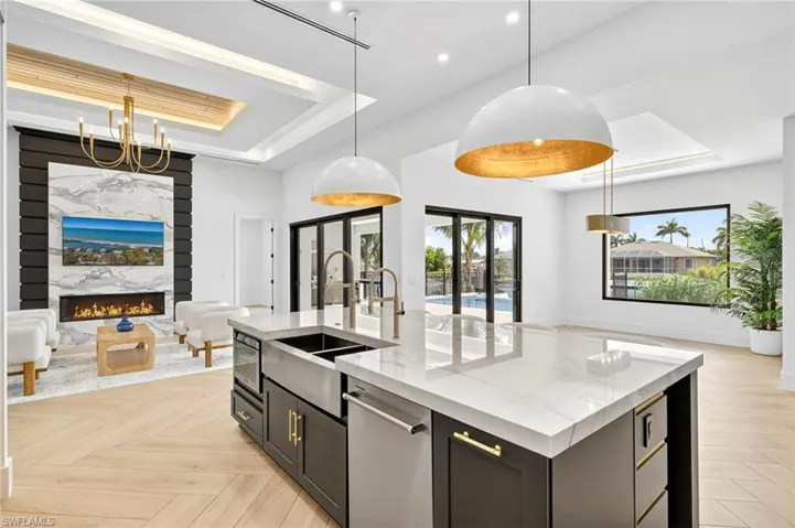 Kitchen featuring a tray ceiling, open floor plan, pendant lighting, light stone countertops, and a fireplace