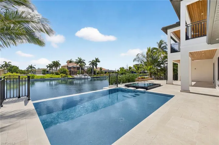View of swimming pool featuring a patio, a water view, a balcony, and a pool with connected hot tub