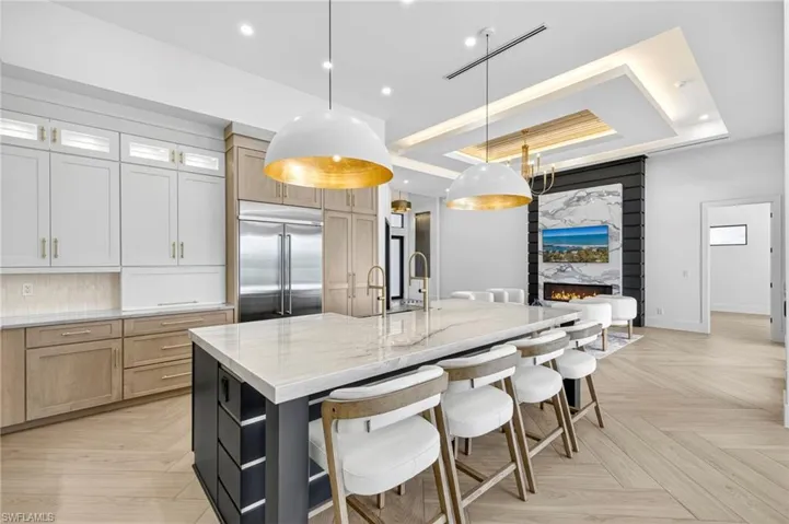 Kitchen with a raised ceiling, light brown cabinetry, a breakfast bar area, a spacious island, and light stone countertops