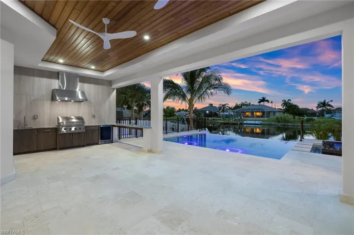 View of pool with an outdoor kitchen, a patio area, a water view, an infinity pool, and ceiling fan