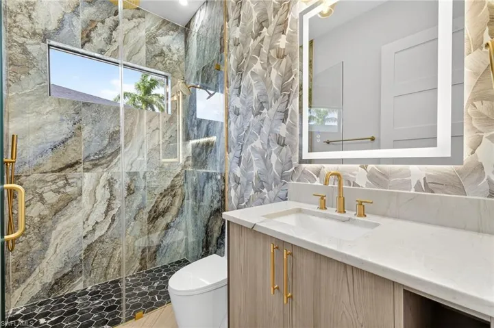 Bathroom featuring plenty of natural light, a marble finish shower, vanity, and tile walls