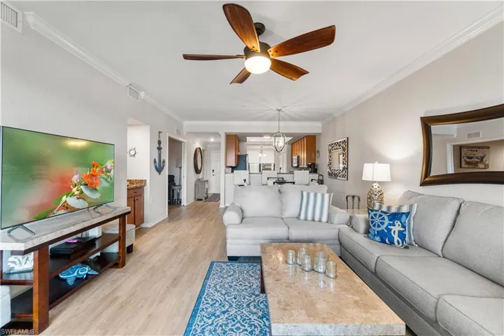Living room featuring ceiling fan with notable chandelier, light wood-type flooring, and ornamental molding