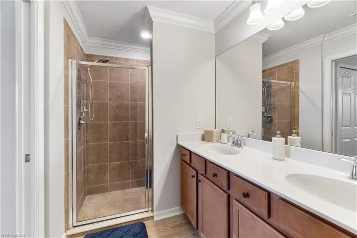 Bathroom with oversized vanity, dual sinks, crown molding, an enclosed shower, and wood-type flooring