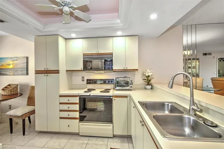 Kitchen featuring sink, a raised ceiling, white range with electric stovetop, light tile patterned flooring, and ornamental molding