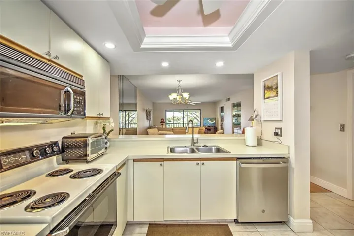 Kitchen with dishwasher, white range with electric cooktop, sink, light tile patterned floors, and a tray ceiling