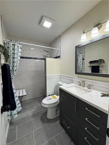 Bathroom featuring vanity, a wainscoted wall, a tile shower, and dark tile patterned floors