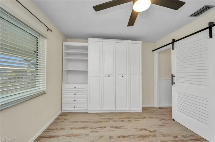 Unfurnished bedroom with a barn door, light wood-style flooring, ceiling fan, and a closet