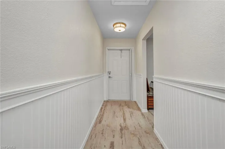 Hallway featuring a textured wall, light wood-style floors, and wainscoting