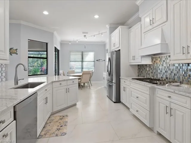Kitchen with light stone countertops, decorative backsplash, appliances with stainless steel finishes, ornamental molding, and white cabinetry