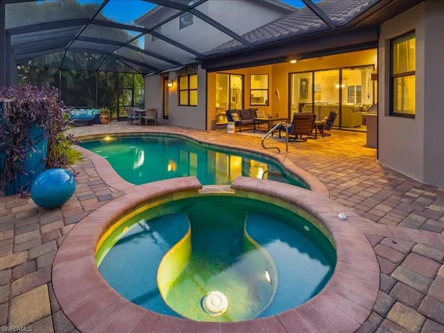 View of pool featuring a sunroom, outdoor lounge area, a pool with connected hot tub, a patio, and glass enclosure