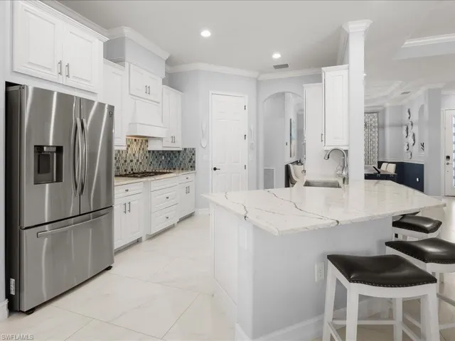 Kitchen with appliances with stainless steel finishes, light stone counters, arched walkways, white cabinets, and crown molding