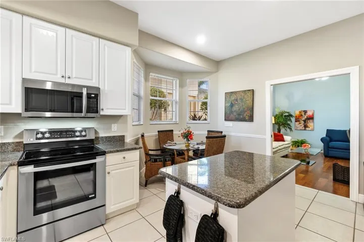 Kitchen with appliances with stainless steel finishes, light tile patterned floors, white cabinetry, and dark stone countertops