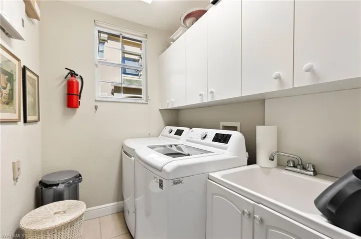 Laundry room featuring sink, light tile patterned floors, cabinets, and independent washer and dryer