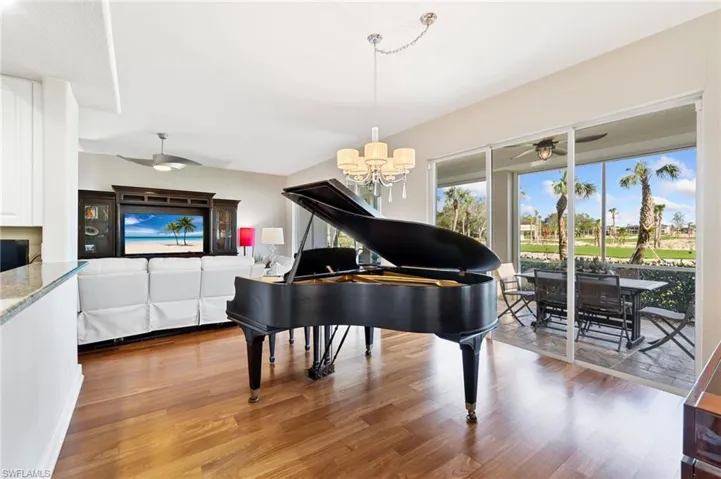 Living room featuring wood flooring, piano and ceiling fan with notable chandelier